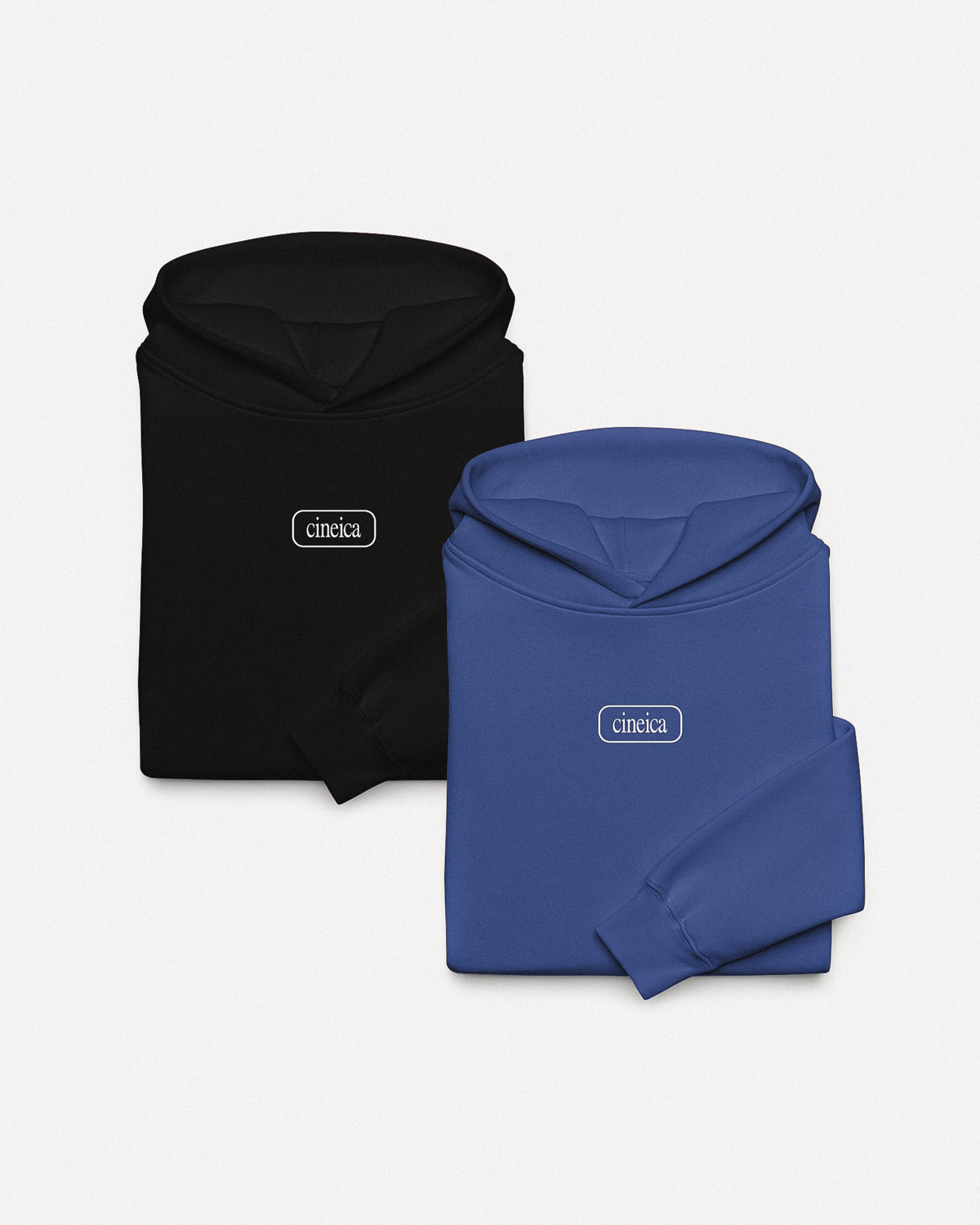 Photo of two folded cineica hoodies. One is black and one is blue. Both feature a framed cineica logo centered on the chest.