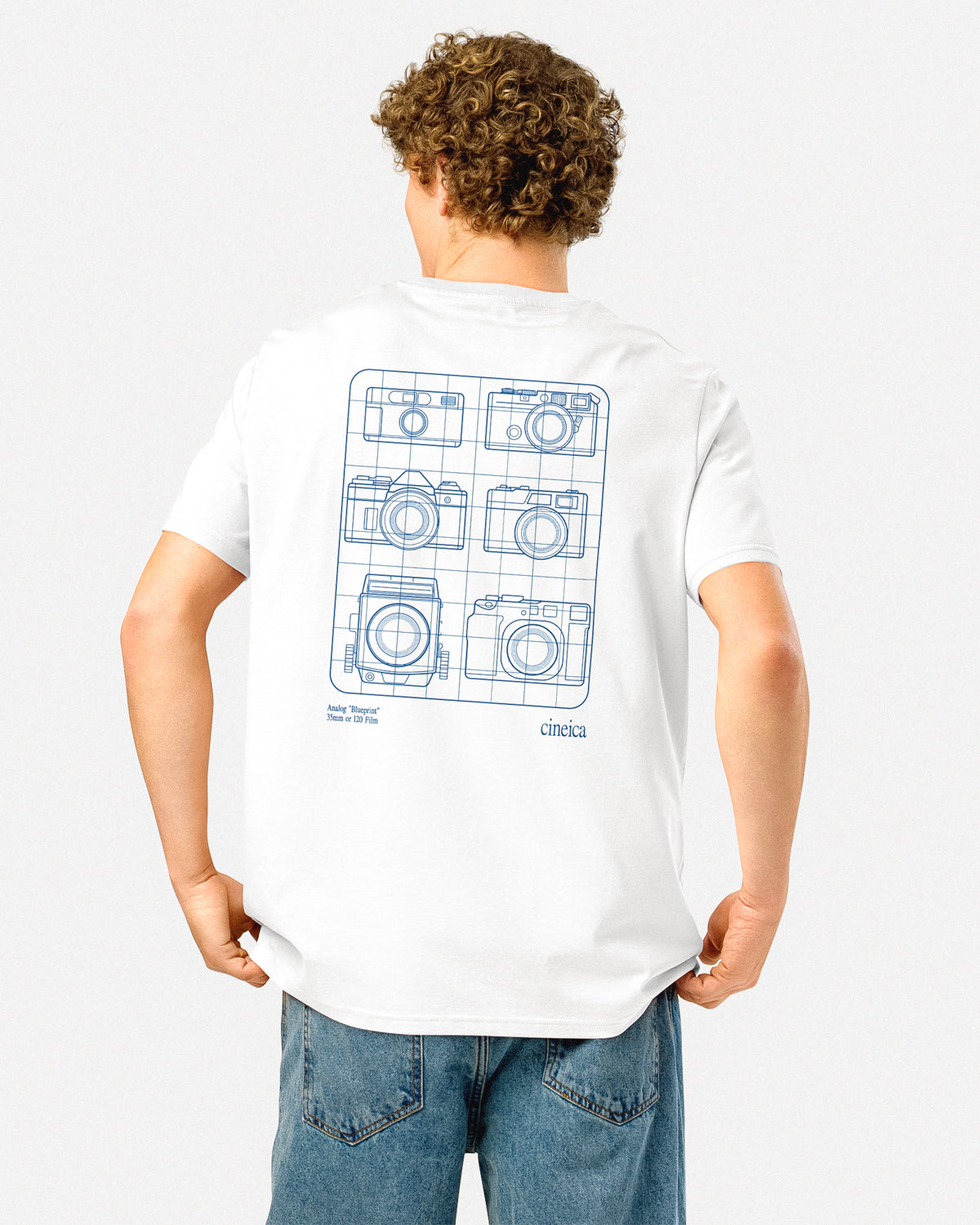 Photo of a man wearing a white cineica t-shirt. The design is in blue and features a "blueprint" of six analog cameras aligned on the back.