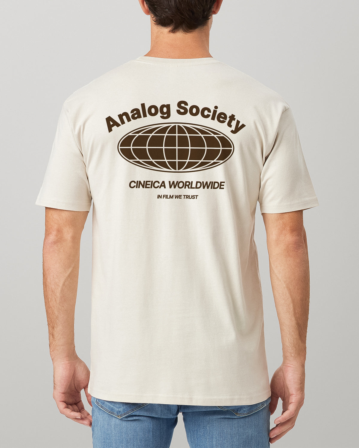 Man wearing a natural beige t-shirt back with analog photography design featuring text "Analog Society", "CINEICA WORLDWIDE", and "IN FILM WE TRUST".