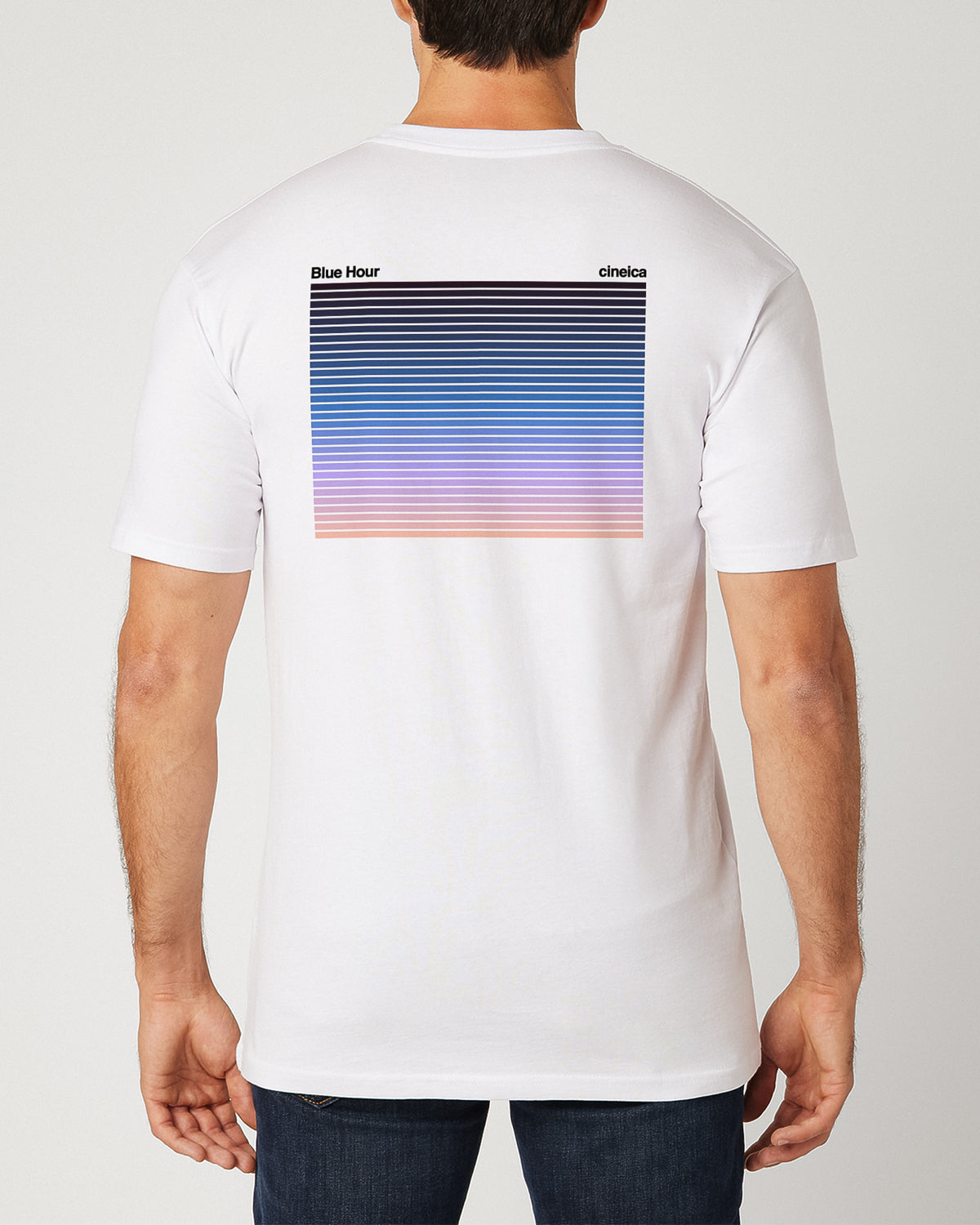 A man wearing a white t-shirt with text "Blue Hour" and "cineica" followed by a gradient of the dusk sky.