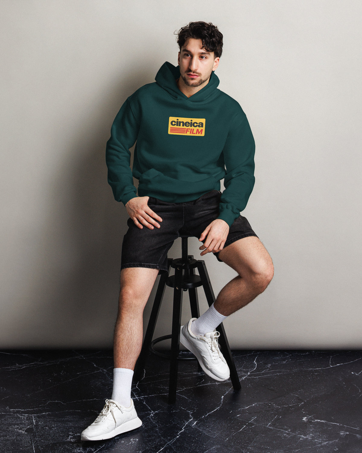 Front of a man wearing a green relaxed hoodie with a vintage retro design with Kodak Film colors and the text "cineica film".