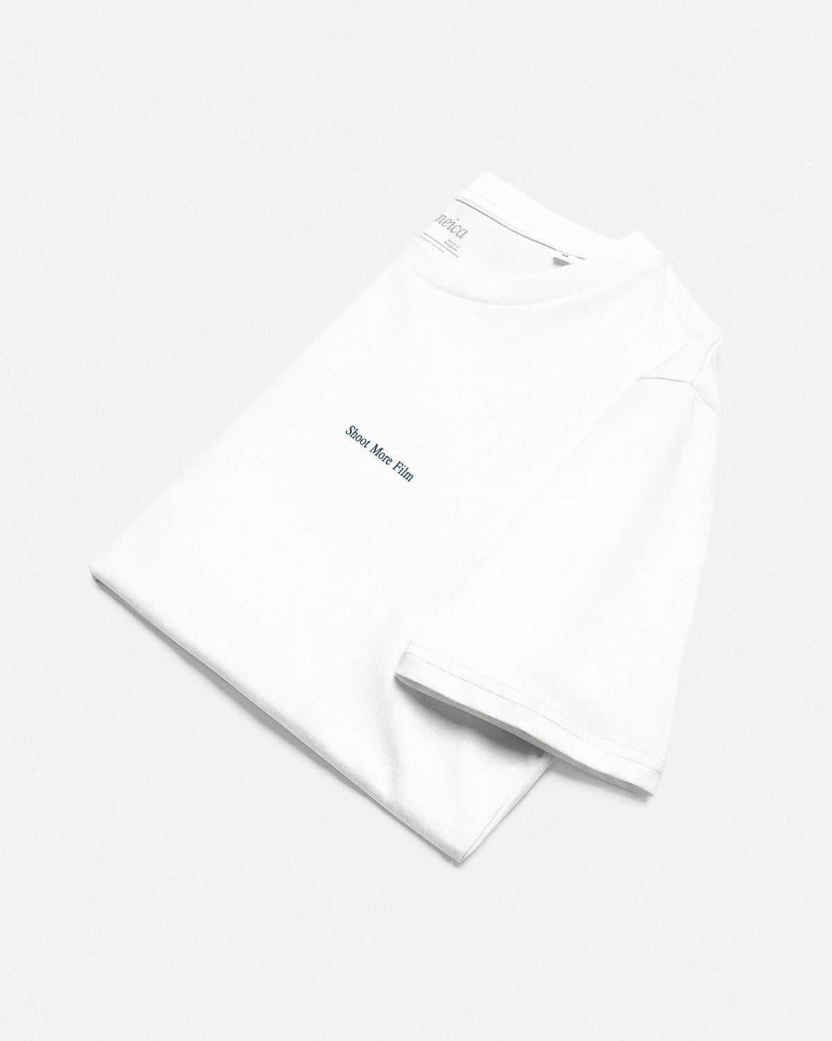 Folded white t-shirt with “Shoot More Film” front design – organic cotton film photography shirt by cineica.